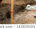 From a close viewpoint, a wooden stake is tied with a red measurement line marking the boundary at a construction site. 143839103