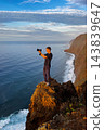 Male photographer works on dramatic cliff near Farol da Ponta do Pargo, Madeira, Portugal. Concept of creative courage, calculated risk, freedom and pursuit of unique perspectives 143839647