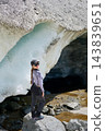 Portrait of female hiker smiles while standing on rock beside massive melting ice cave at Aletsch Glacier, surrounded by blue glacial ice in Swiss Alps, Switzerland 143839651