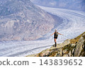 Back view of female hiker spreads arms while balancing on rocky viewpoint above Aletsch Glacier, expressing freedom, wellbeing and achievement during active summer adventure in Swiss Alps, Switzerland 143839652