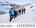 Rear view of hiking group trekking uphill across snowy slope, surrounded by rugged rock, winter mountains and bright Arctic light in Lofoten Islands, Northern Norway 143839669