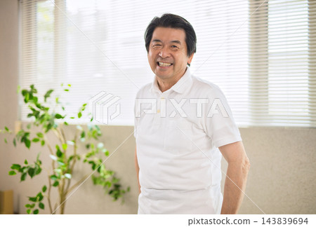 一位面帶微笑的老先生站在窗邊。 一位面帶微笑的老先生站在窗邊。 143839694