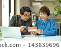 A couple in their 60s looking at their savings passbook in the living room 143839696