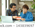 A couple in their 60s looking at their savings passbook in the living room 143839697
