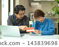 A couple in their 60s looking at their savings passbook in the living room 143839698