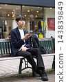 A male businessman in his twenties sitting on a bench and looking at his smartphone 143839849