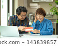 A couple in their 60s looking at their savings passbook in the living room 143839857