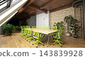 A modern conference room featuring a long wooden table, bright green chairs, an exposed brick wall, and potted plants. 143839928
