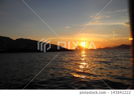 Sunset behind isolated rocky islet in Adriatic Sea with golden light on water Sunset behind isolated rocky islet in Adriatic Sea with golden light on water 143841222