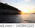 Bright sunburst sunset behind rocky Mediterranean island with seagull in flight 143841225