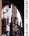 Old weathered wrought iron fence or gate featuring classic decorative scrolls and sharp spearhead finials. Dark corroded metal surface with textures of rust and age 143841280