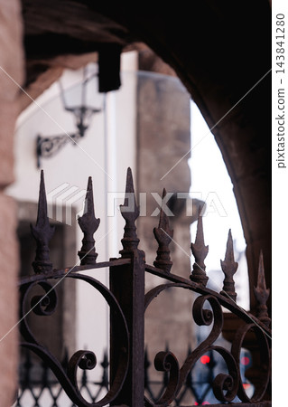 Old weathered wrought iron fence or gate featuring classic decorative scrolls and sharp spearhead finials. Dark corroded metal surface with textures of rust and age Old weathered wrought iron fence or gate featuring classic decorative scrolls and sharp spearhead finials. Dark corroded metal surface with textures of rust and age 143841280