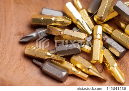 Heap of metallic steel and golden titanium screwdriver bits on a natural wooden background Heap of metallic steel and golden titanium screwdriver bits on a natural wooden background 143841286