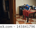Focused woman tailor measures, marks and cuts red fabric for handmade clothing at a sewing table in her warm home tailoring workshop 143841796