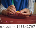 Hands pull sewing thread through beeswax over marked fabric while preparing materials for garment construction in a textile workshop 143841797