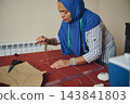 Sewing and measuring red fabric for handmade clothing, woman tailor works in a home tailoring workshop with paper garment patterns 143841803