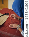 Headscarf woman stitches rust-colored fabric by hand with a needle and white thread for handmade garment construction indoors 143841804