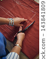 Tailor cuts red fabric with scissors along a chalk pattern line during handmade clothing production in a home sewing workshop 143841809