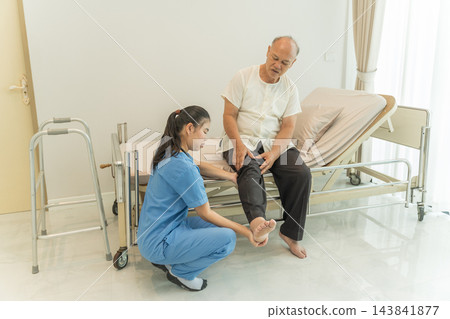 Nurse assisting senior man with leg pain at home for better mobility 143841877