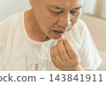 Senior man taking medication with water for health management at home. 143841911