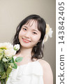 A young Japanese woman in her 20s, wearing a wedding dress and holding a bouquet, looking at the camera; wedding, bridal 143842405