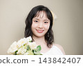 A young Japanese woman in her 20s, wearing a wedding dress and holding a bouquet, looking at the camera; wedding, bridal 143842407