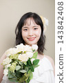 A young Japanese woman in her 20s, wearing a wedding dress and holding a bouquet, looking at the camera; wedding, bridal 143842408