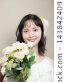A young Japanese woman in her 20s, wearing a wedding dress and holding a bouquet, looking at the camera; wedding, bridal 143842409