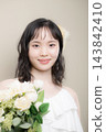 A young Japanese woman in her 20s, wearing a wedding dress and holding a bouquet, looking at the camera; wedding, bridal 143842410