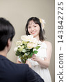 A young Japanese bride, wearing a wedding dress and holding a white bouquet, smiles happily at the groom at their wedding. 143842725