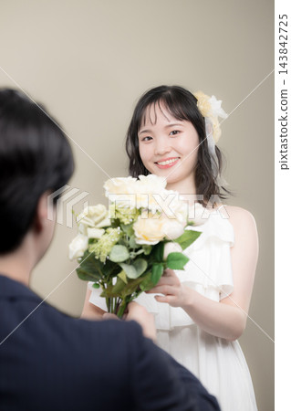 婚禮上,一位年輕的日本新娘穿著婚紗,手捧白色花束,幸福地對著新郎微笑。 婚禮上,一位年輕的日本新娘穿著婚紗,手捧白色花束,幸福地對著新郎微笑。 143842725