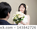 A young Japanese bride, wearing a wedding dress and holding a white bouquet, smiles happily at the groom at their wedding. 143842726
