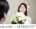 A young Japanese bride, wearing a wedding dress and holding a white bouquet, smiles happily at the groom at their wedding. 143842727