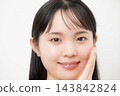 A young woman, appearing to be in her teens or twenties, with her hand on her cheek against a white background, smiling and looking directly at the camera in a beauty/glamour photo. 143842824