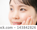 A close-up of a young woman, likely in her teens or twenties, with her hand on her cheek against a white background, focusing on her eyelashes and beauty. 143842826