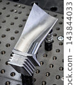 A machined metal turbine blade is positioned on a perforated worktable 143844033