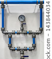 Blue plastic and metal pipe assembly with gauge mounted on an indoor wall 143844034