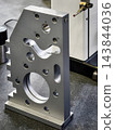 Machined metal inspection plate positioned beside a measuring probe in a workshop 143844036