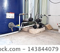 Residential water pump station featuring pressure controller unit attached to electric pump with pvc piping infrastructure for domestic water supply. 143844079
