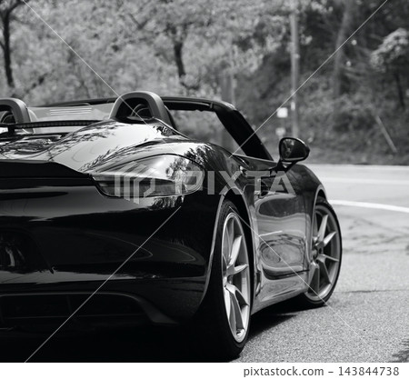 一輛線條流暢的黑色保時捷Boxster Spyder跑車,以及一條蜿蜒的道路,路上有明顯的維修痕跡。 一輛線條流暢的黑色保時捷Boxster Spyder跑車,以及一條蜿蜒的道路,路上有明顯的維修痕跡。 143844738