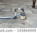 White PVC pipe construction forming loop above ground pump mechanism with blue electrical cable wire for water supply utility in outdoor setting. 143844949