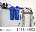 Two bright blue water filter cartridges with electrical connections and PVC pipes for residential water purification setup. 143844952