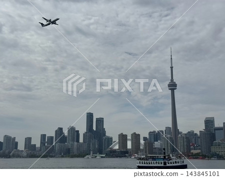 Toronto, Canada Airplane flying over Toronto skyline and ferry boat on water, cloudy sky and urban Toronto, Canada Airplane flying over Toronto skyline and ferry boat on water, cloudy sky and urban 143845101