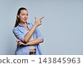 Young woman pointing finger at copy space in studio on gray background 143845963