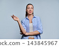 Confident young woman gesturing with hand towards copy space on grey background 143845967