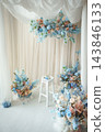 Light photo studio interior set with blue floral arch, curtain backdrop and white wooden chair 143846133
