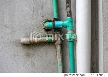 Green PPR plastic water pipes connected to a concrete wall outdoor structure. Plumbing installation and drainage pipeline for residential building. 143847042