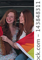 Vertical video. Young lesbian couple taking selfie and sit in the back of the car. Two happy girlfriends pose with rainbow flag. Lgbt woman, showing love to. 143848311