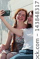Vertical video. Young adult lesbian couple taking selfie in the city. Two happy girlfriends pose with rainbow flag. Lgbt woman, showing love to each other. 143848317
