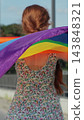 Vertical video. Back view of young Woman holding LGBT rainbow flag while walking on street on a sunny day. 143848321